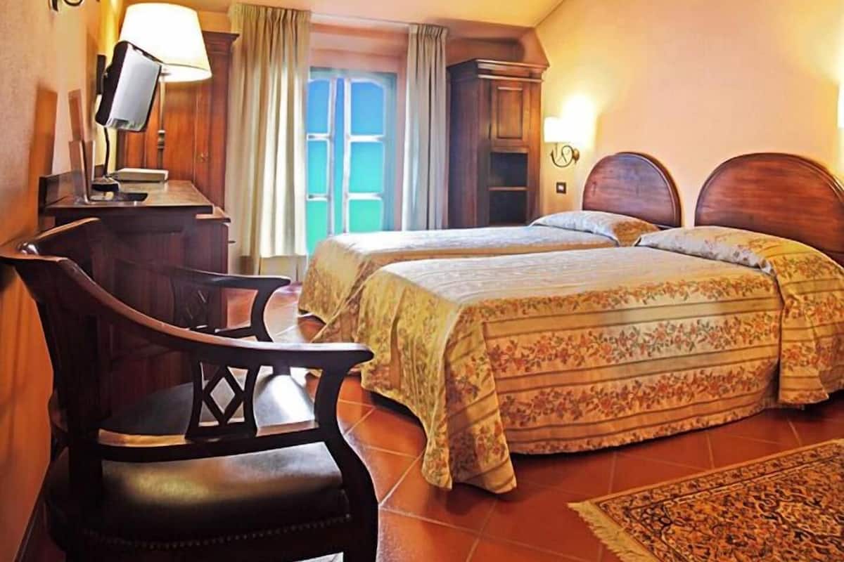 Une chambre avec deux lits, un bureau, une chaise et une fenêtre avec des rideaux.