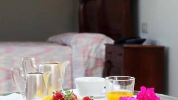 Colazione servita con un boccale, un piatto di frutta, un bicchiere di succo d'arancia e un letto sullo sfondo.