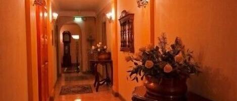 Un pasillo con piso de madera, una planta en maceta con flores y apliques de pared.