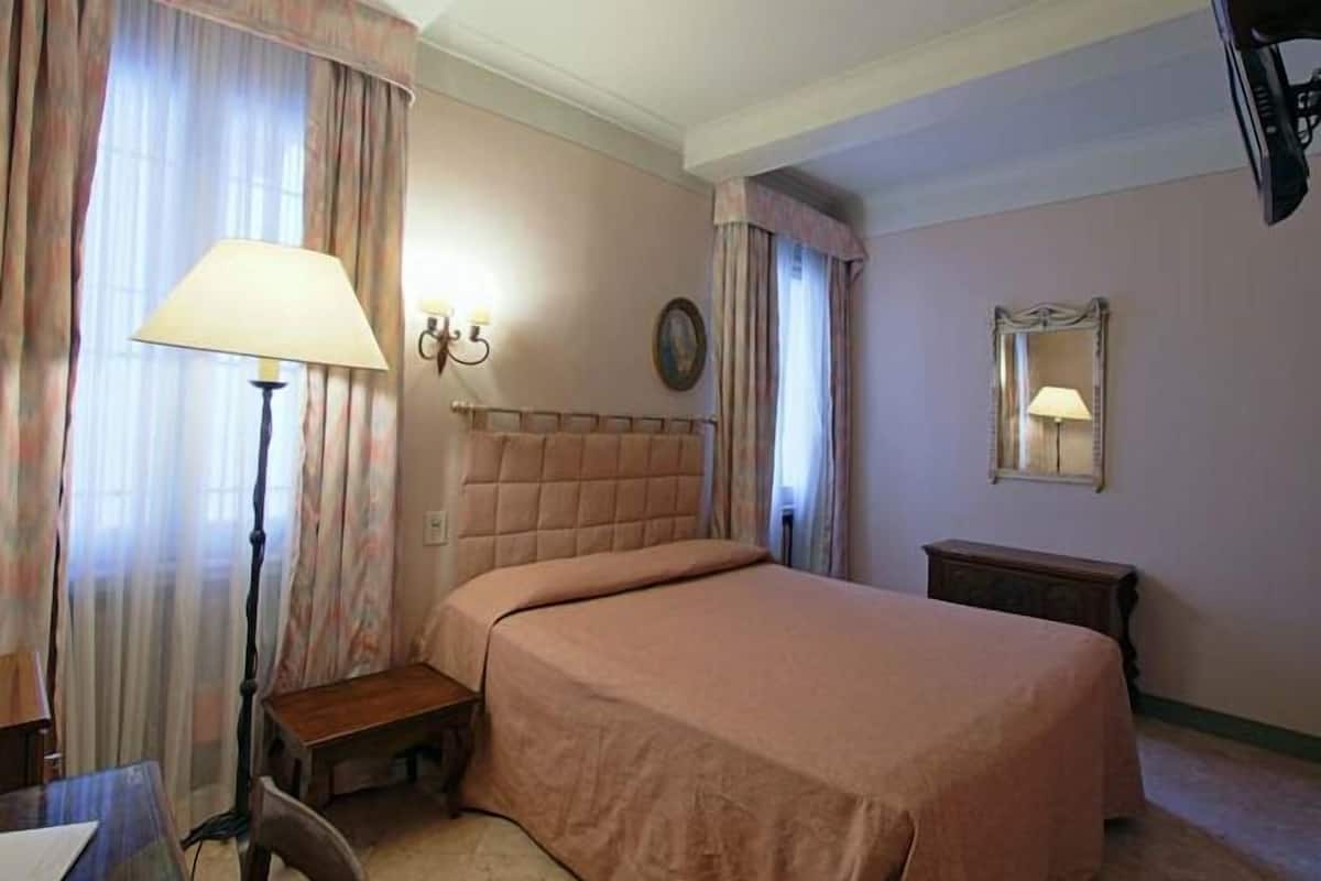 Une chambre d’hôtel avec un lit, un bureau, une lampe et un miroir.