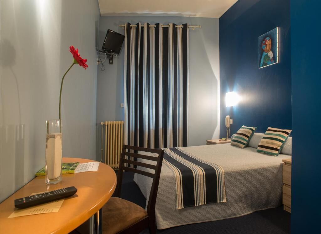 Un dormitorio con cama, mesita de noche, silla y televisor montado en la pared.