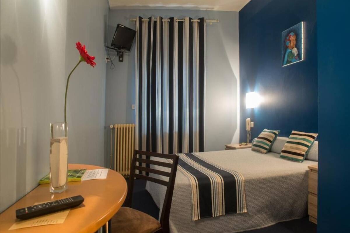 A bedroom with a bed, bedside table, chair, and a TV mounted on the wall.