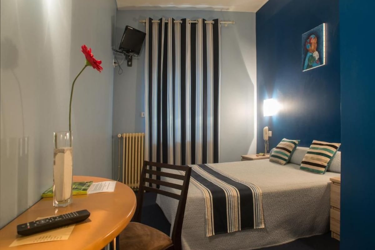 Un dormitorio con cama, mesita de noche, silla y televisor montado en la pared.