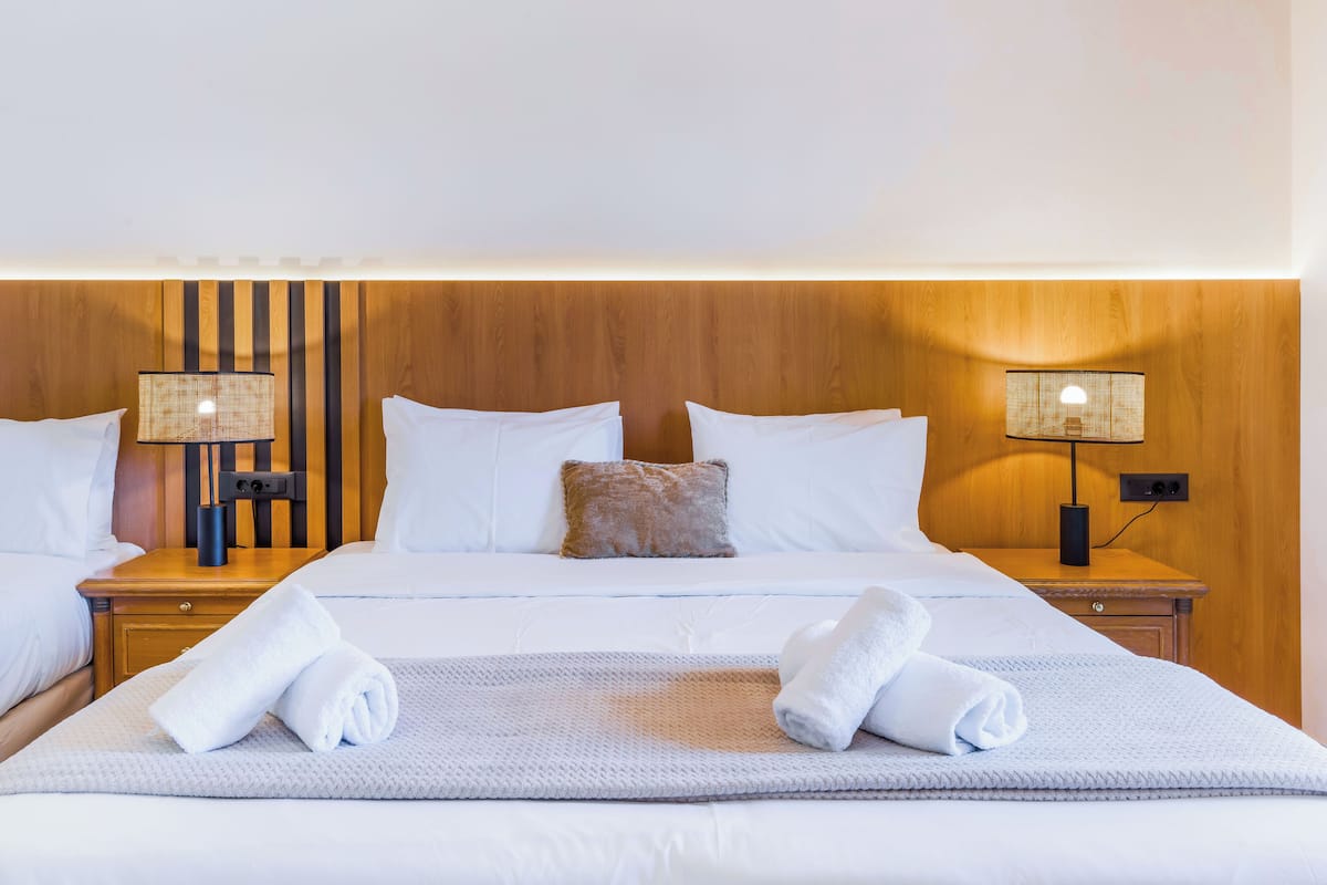 A hotel room with a large bed, two bedside tables, a wooden headboard, and two wall-mounted lamps.