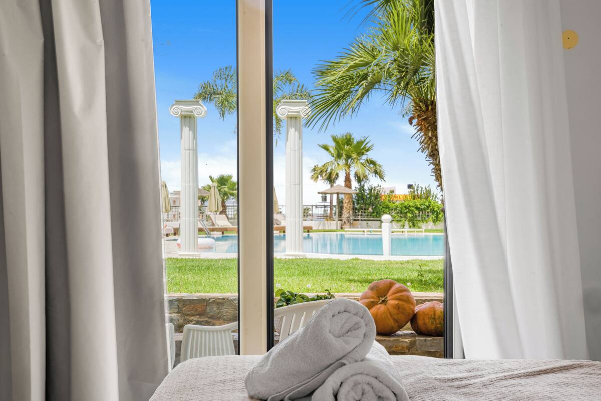 A hotel room with a view of a swimming pool, palm trees, and a gazebo.