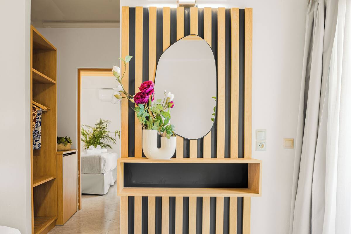 A modern bathroom with a wooden vanity, a mirror, and a vase with flowers.