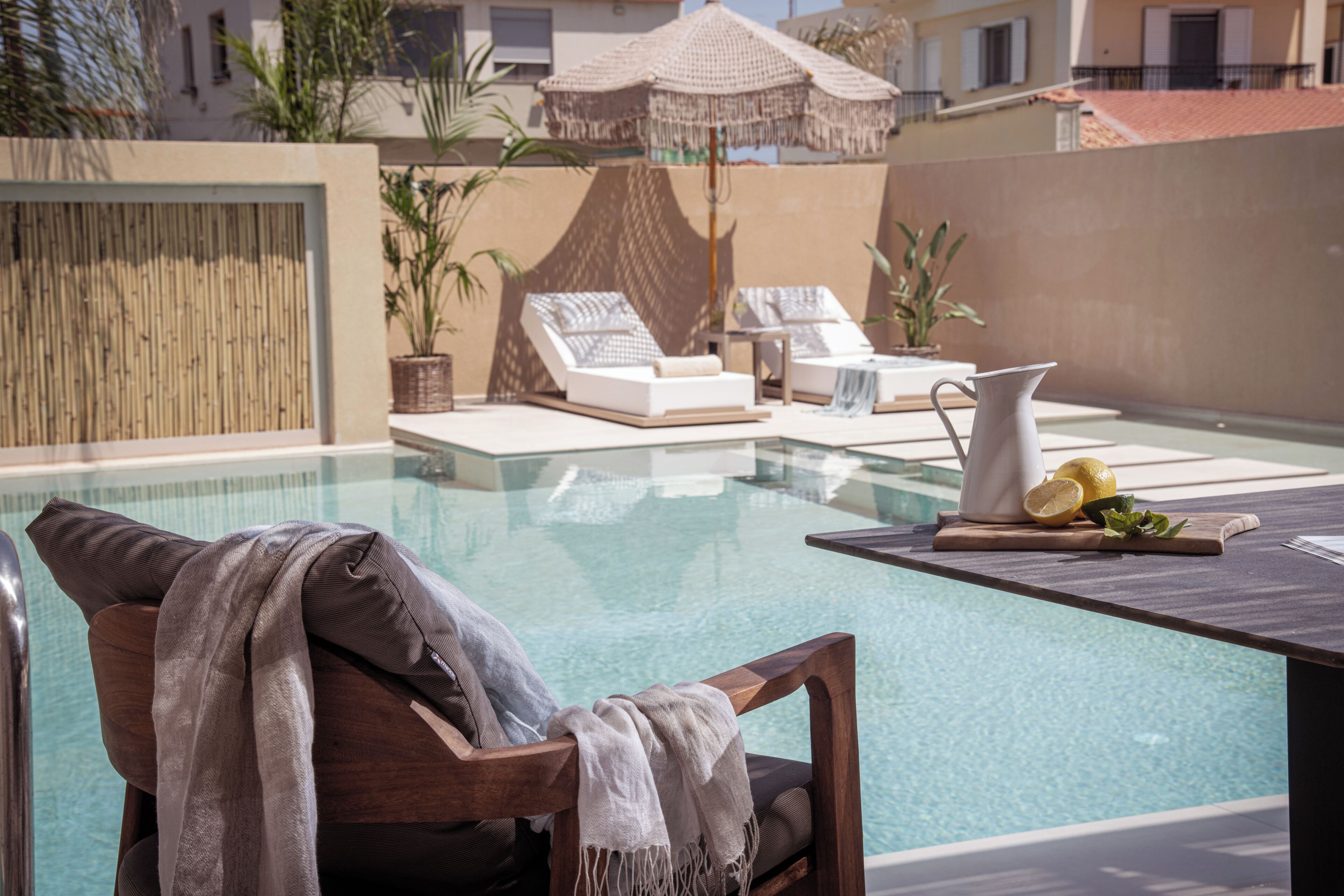 Zona junto a la piscina con sillones de descanso, una mesa con jarras y limones, y vista a la piscina.