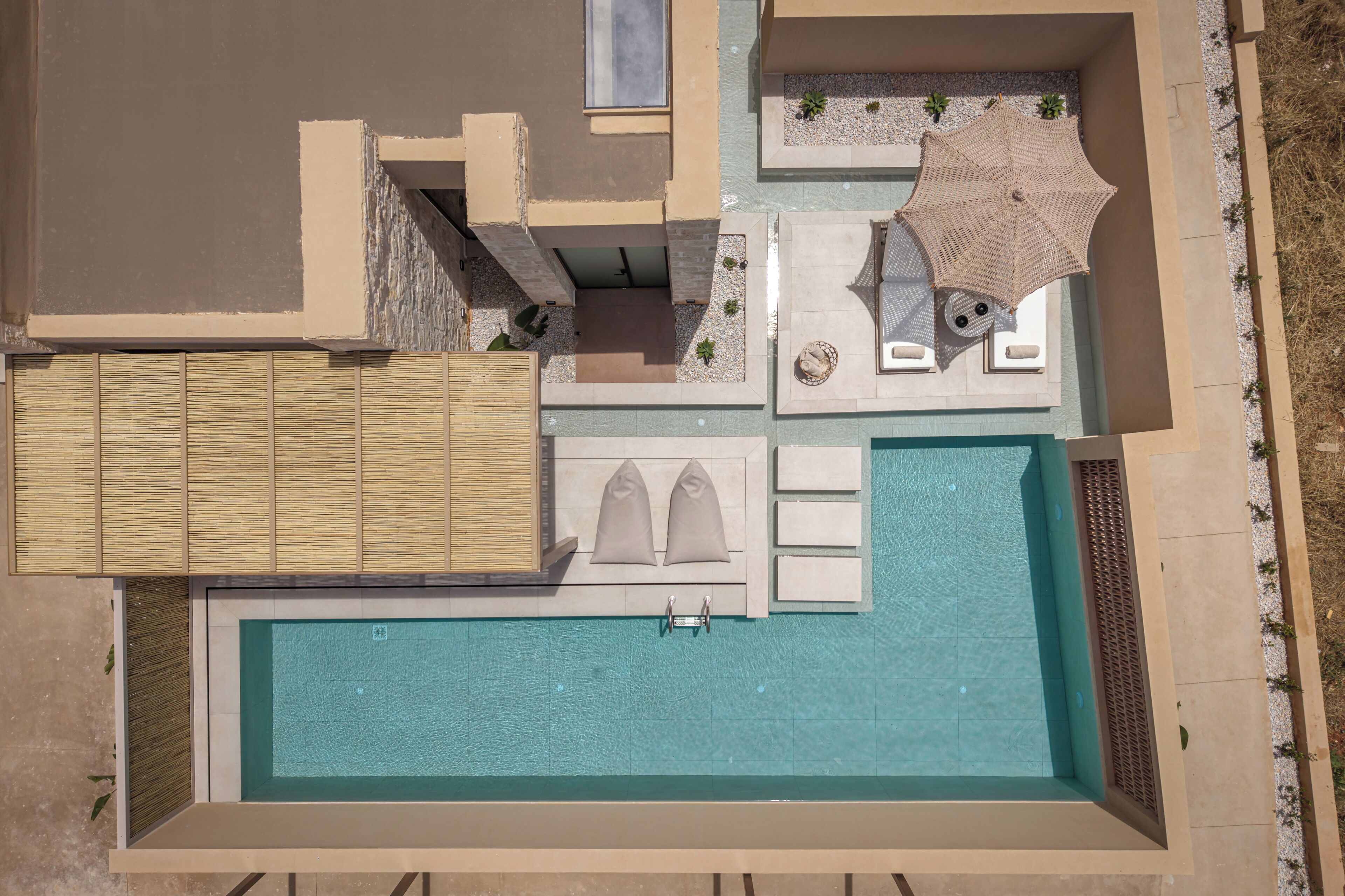 An aerial view of a swimming pool area with lounge chairs, a sun umbrella, and a small garden area.