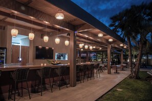 An outdoor bar area with multiple hanging lights, a flat-screen TV, and a variety of seating options. - Socrates Hotel Malia Beach (Hersonissos)