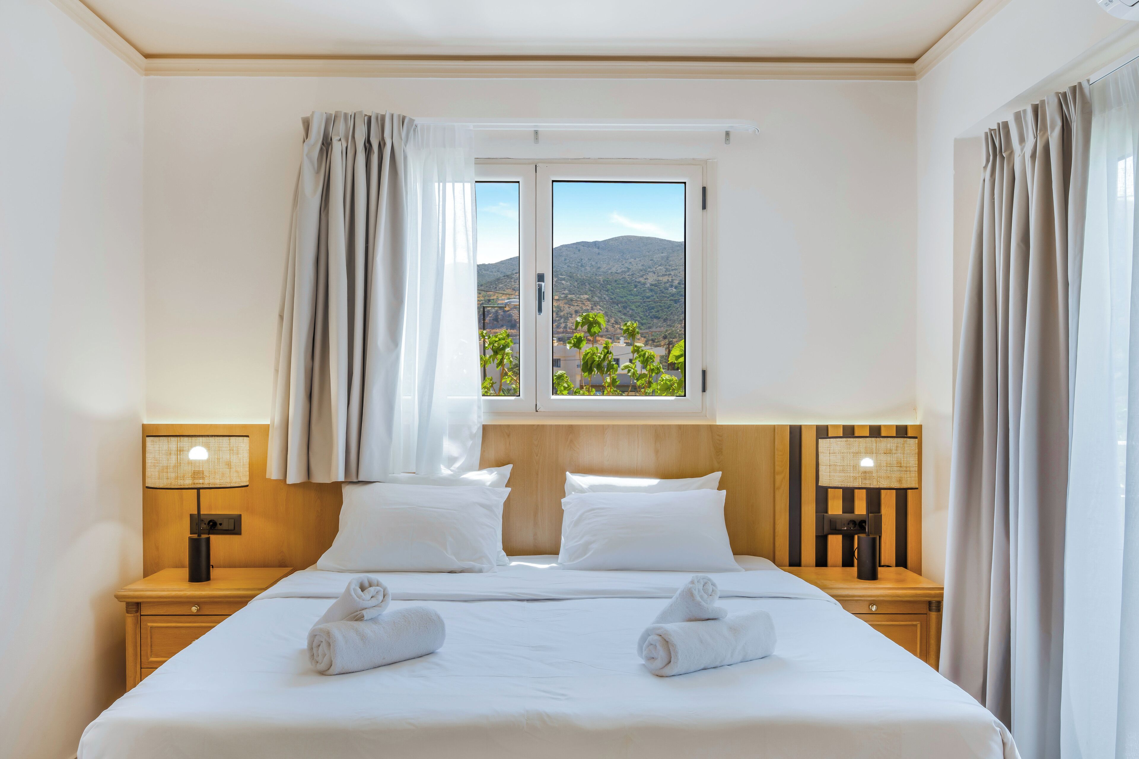 A hotel room with a bed, two nightstands, a window with curtains, and a view of a mountainous landscape.