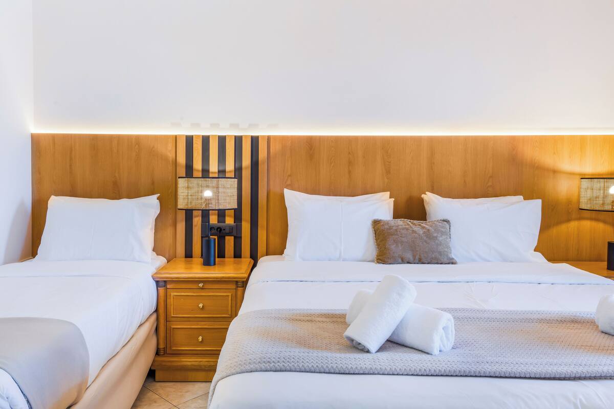 A hotel room with two beds, wooden headboard, bedside lamps, and a small table.