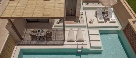 A rooftop pool area with a lounge, umbrellas, and a table with chairs.