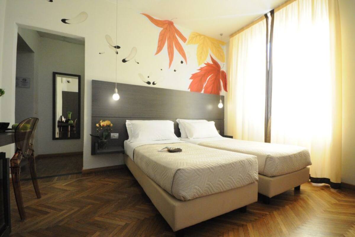 Une chambre d’hôtel avec deux lits, un plancher en bois, un luminaire fixé au mur et un miroir.