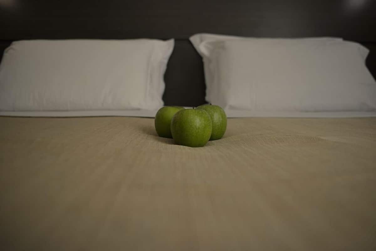 Un lit avec des oreillers blancs et une pomme verte posée sur le dessus.