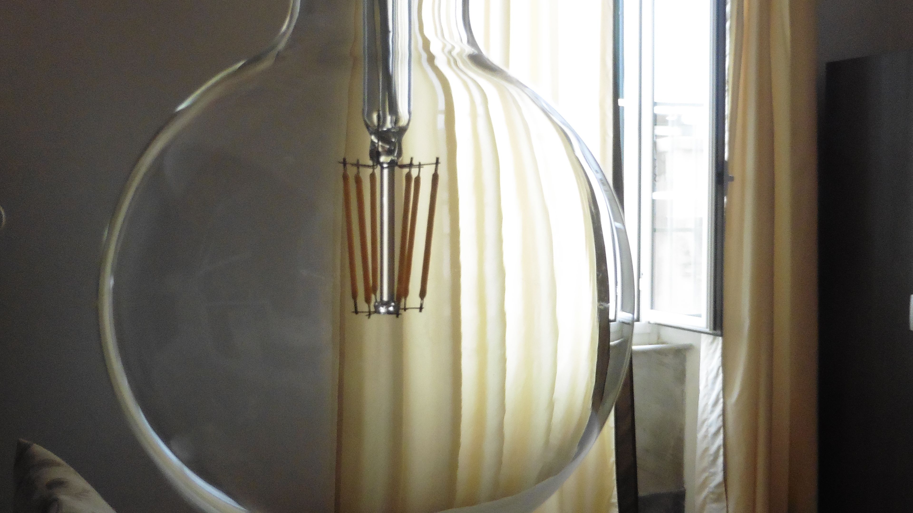 A room with a large, round mirror reflecting a window with vertical blinds.