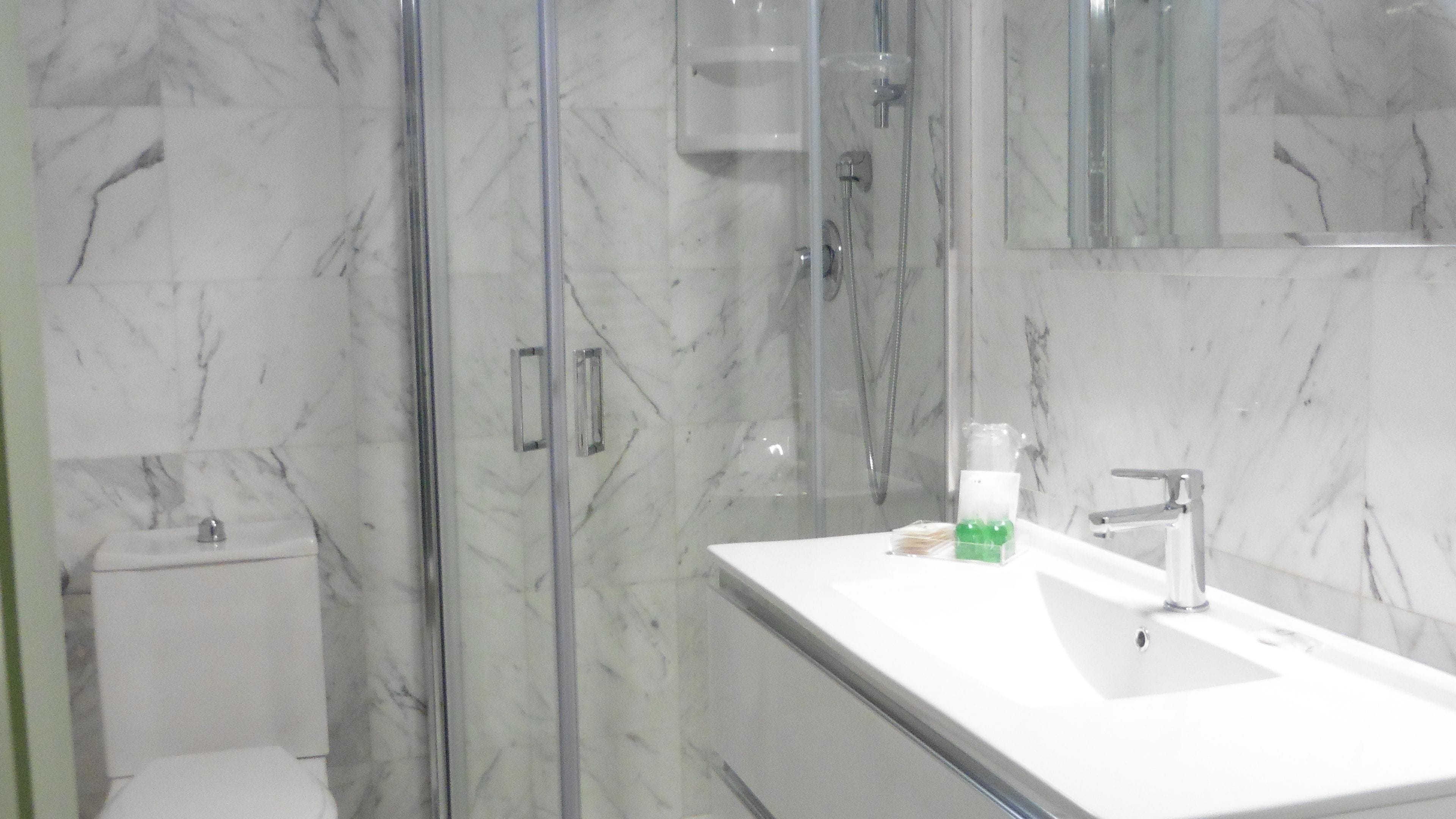 A modern bathroom with a glass shower enclosure, a white sink, and a marble backsplash.