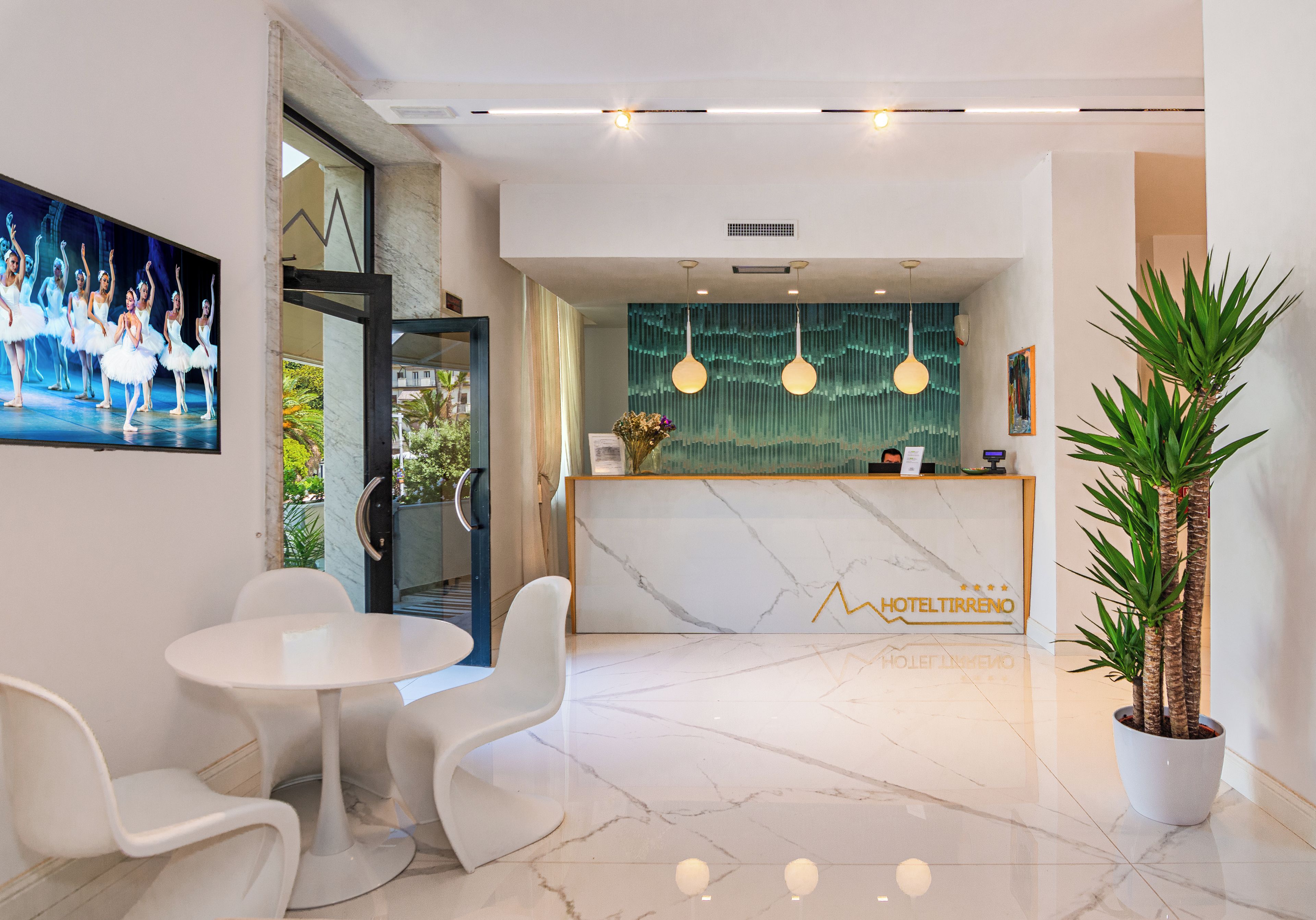 Zona de recepción de un hotel con suelo de mármol, mostrador de recepción y un cuadro grande de bailarines.