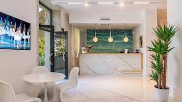 Zona de recepción de un hotel con suelo de mármol, mostrador de recepción y un cuadro grande de bailarines.