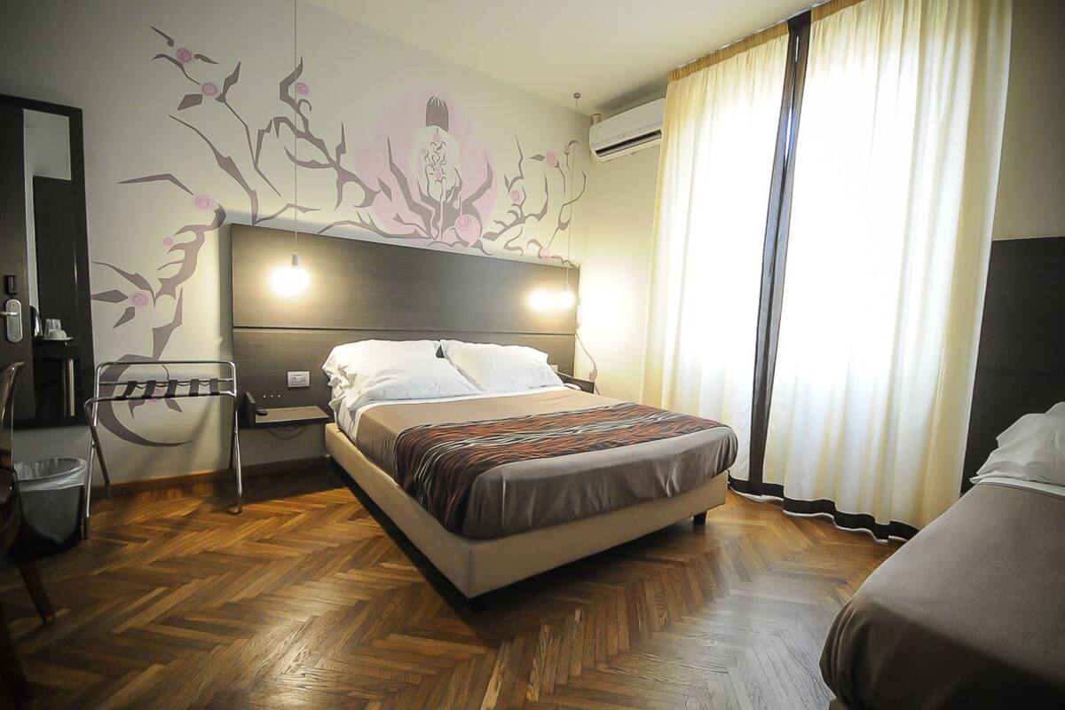 Une chambre d’hôtel comprenant un lit, une table de chevet, une chaise et un climatiseur fixé au mur.