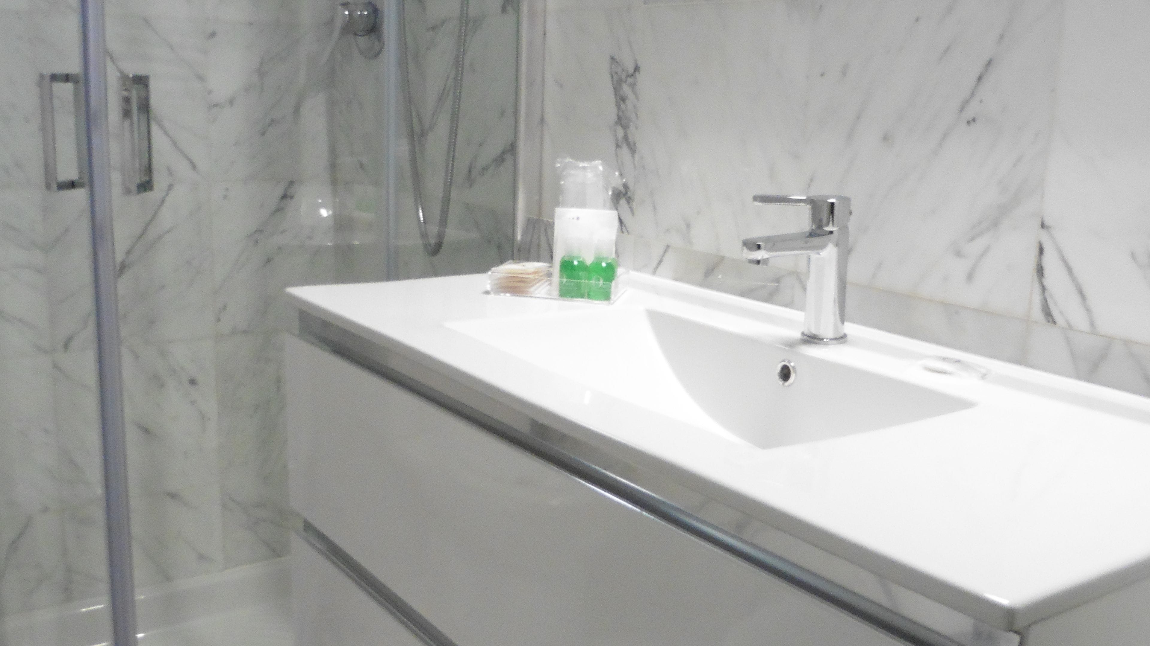 A bathroom with a white sink, a glass shower enclosure, and a marble wall.