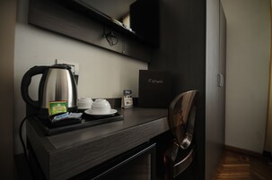 Una habitación de hotel moderna con un escritorio de madera oscura, una tetera, una cápsula de café y una cápsula de té, además de un minibar.
