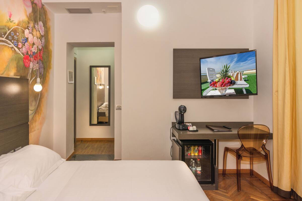 Une chambre d’hôtel équipée d’un lit, d’un bureau avec une chaise, d’une télévision et d’un mini-bar.