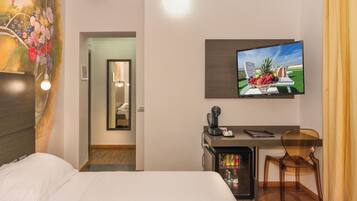 Quarto de hotel com uma cama, uma escrivaninha com cadeira, televisão e um minibar.