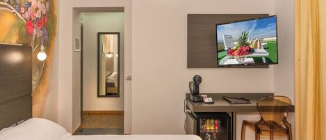 Ein Hotelzimmer mit einem Bett, einem Schreibtisch mit Stuhl, einem Fernseher und einer Minibar.