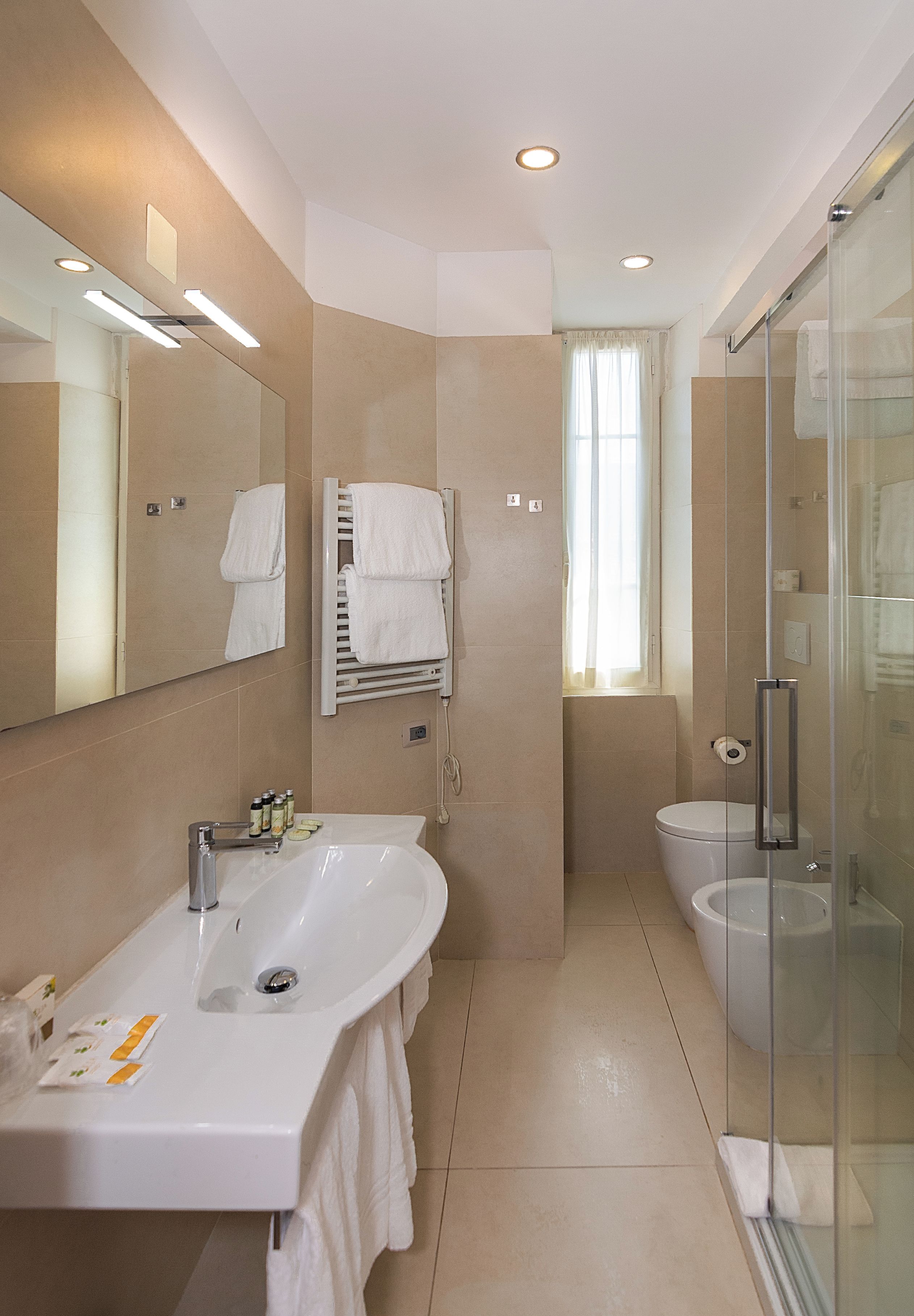 Un baño moderno con un espejo grande, un lavabo, un inodoro y una ducha con paredes de vidrio.