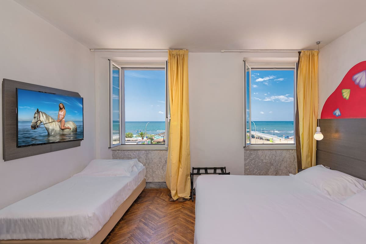Une chambre d’hôtel avec deux lits, une grande fenêtre donnant sur la plage et un tableau représentant un cheval accroché au mur.