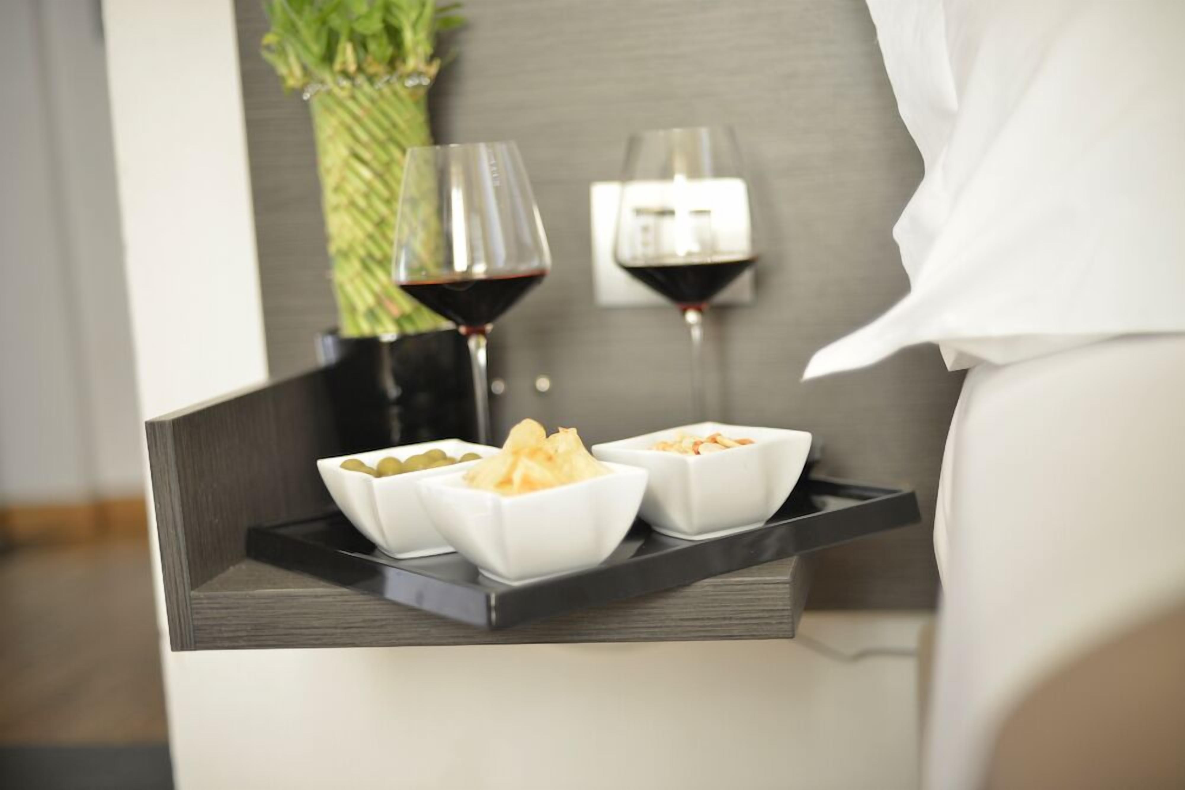 Una bandeja con aperitivos en recipientes y dos copas de vino tinto sobre una mesita de noche.