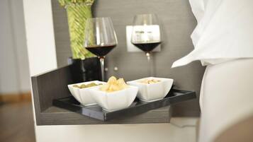 Una bandeja con aperitivos en recipientes y dos copas de vino tinto sobre una mesita de noche.
