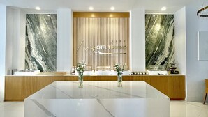 Un área de recepción de hotel moderna con paredes de mármol, un mostrador de recepción central y una barra de madera.