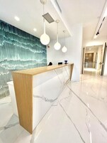 Una moderna recepción con encimera de mármol y detalles de madera, frente a una pared azul con textura.