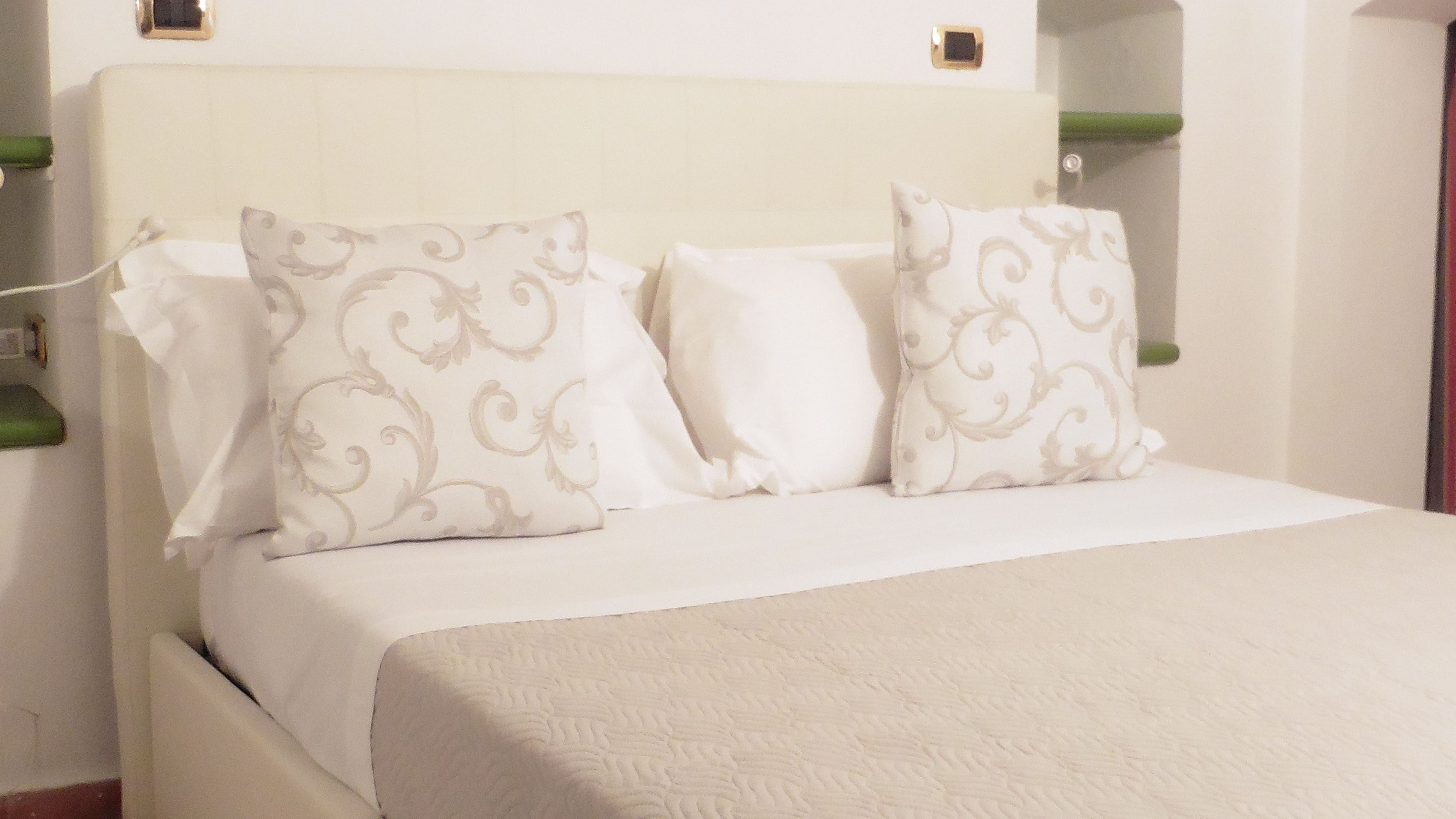 Un lit avec une tête de lit blanche, deux coussins décoratifs et un couvre-lit blanc.