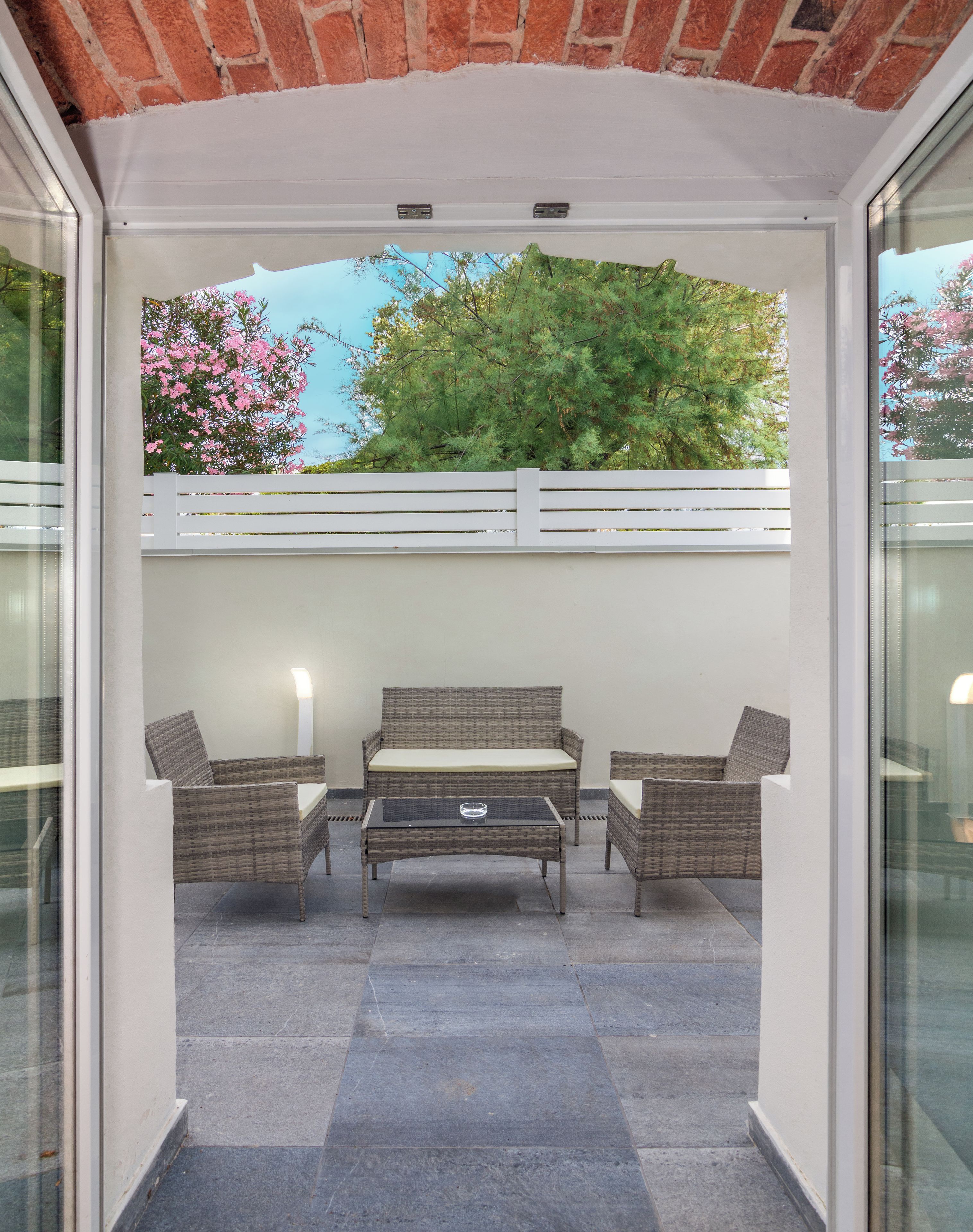 Un patio al aire libre con un conjunto de sofá de mimbre, una mesa y una valla blanca.