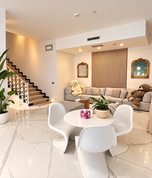 A modern living room with a staircase, a sofa set, two white chairs, a round table, and decorative elements like a mirror and plants. - Hotel Tirreno (Massa)