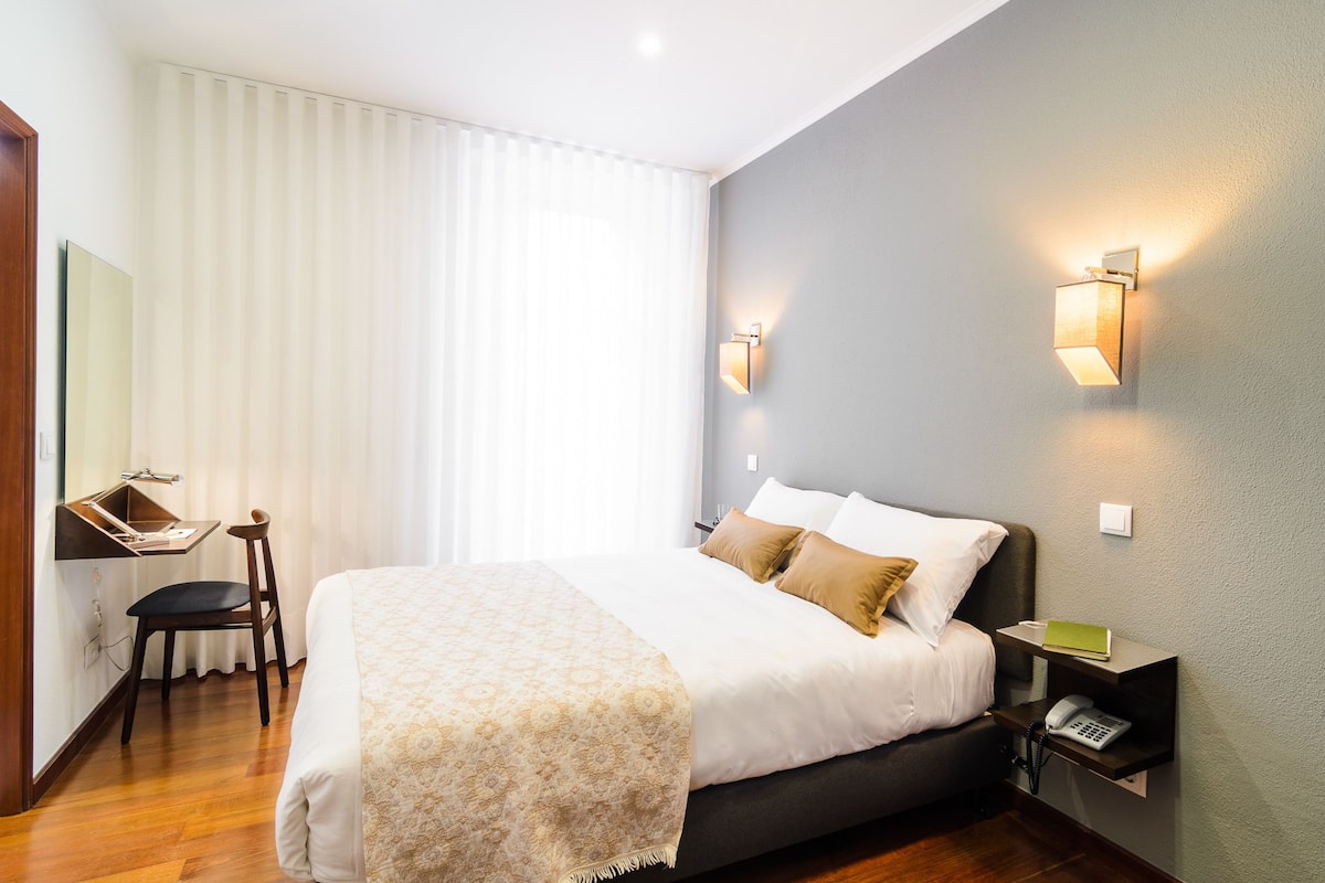 Une chambre d’hôtel comprenant un lit, une table de chevet, une lampe et un bureau avec une chaise.