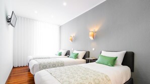 Habitación de hotel con dos camas, un ventanal grande con cortinas blancas e iluminación empotrada.
