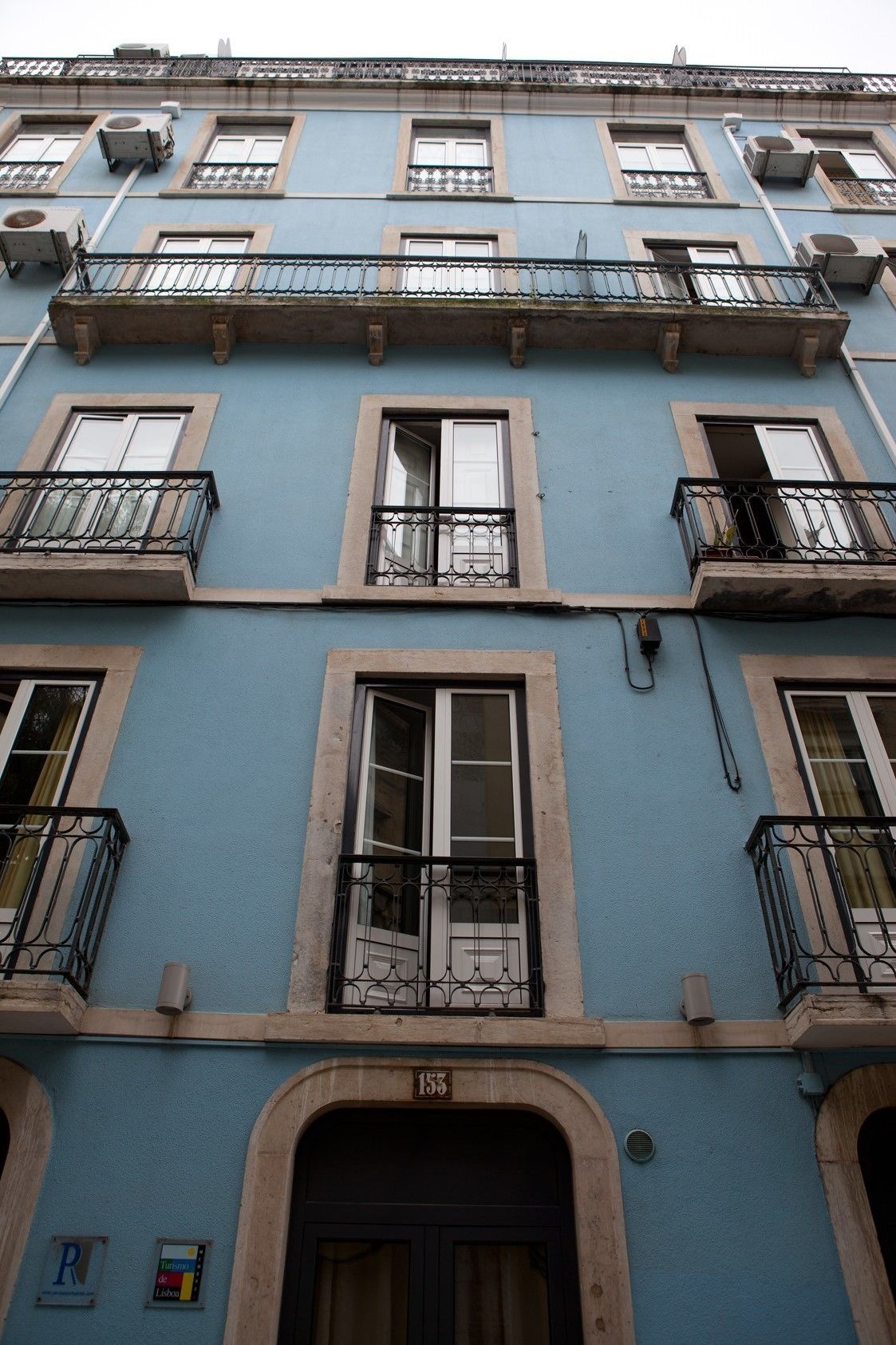 A multi-story building with balconies, a central entrance with an arch, and a visible door number.