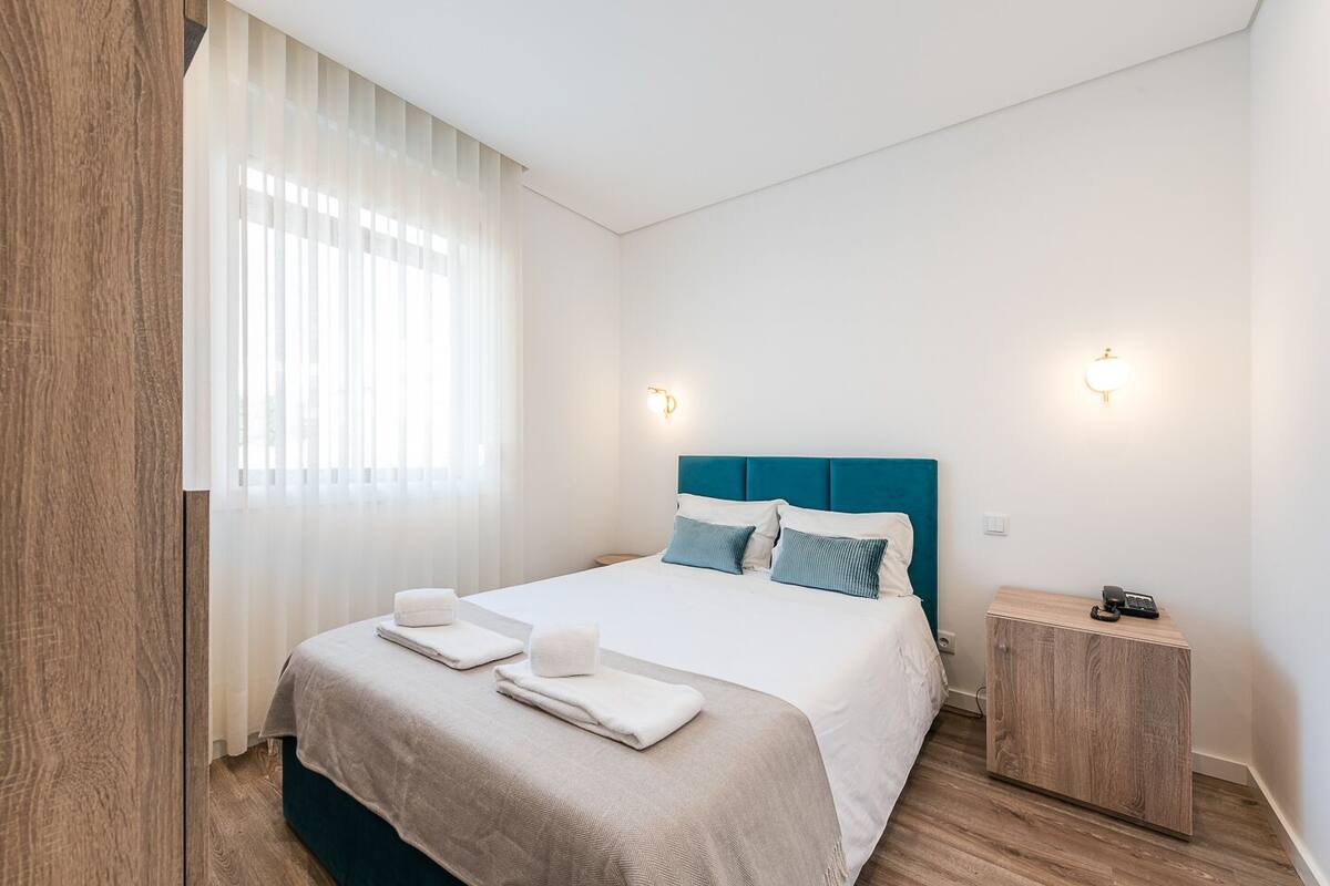 A modern hotel room with a large bed, white linens, a blue headboard, and two bedside lamps.