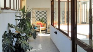 Un couloir doté d’un sol carrelé, de grandes fenêtres et de plantes en pot.