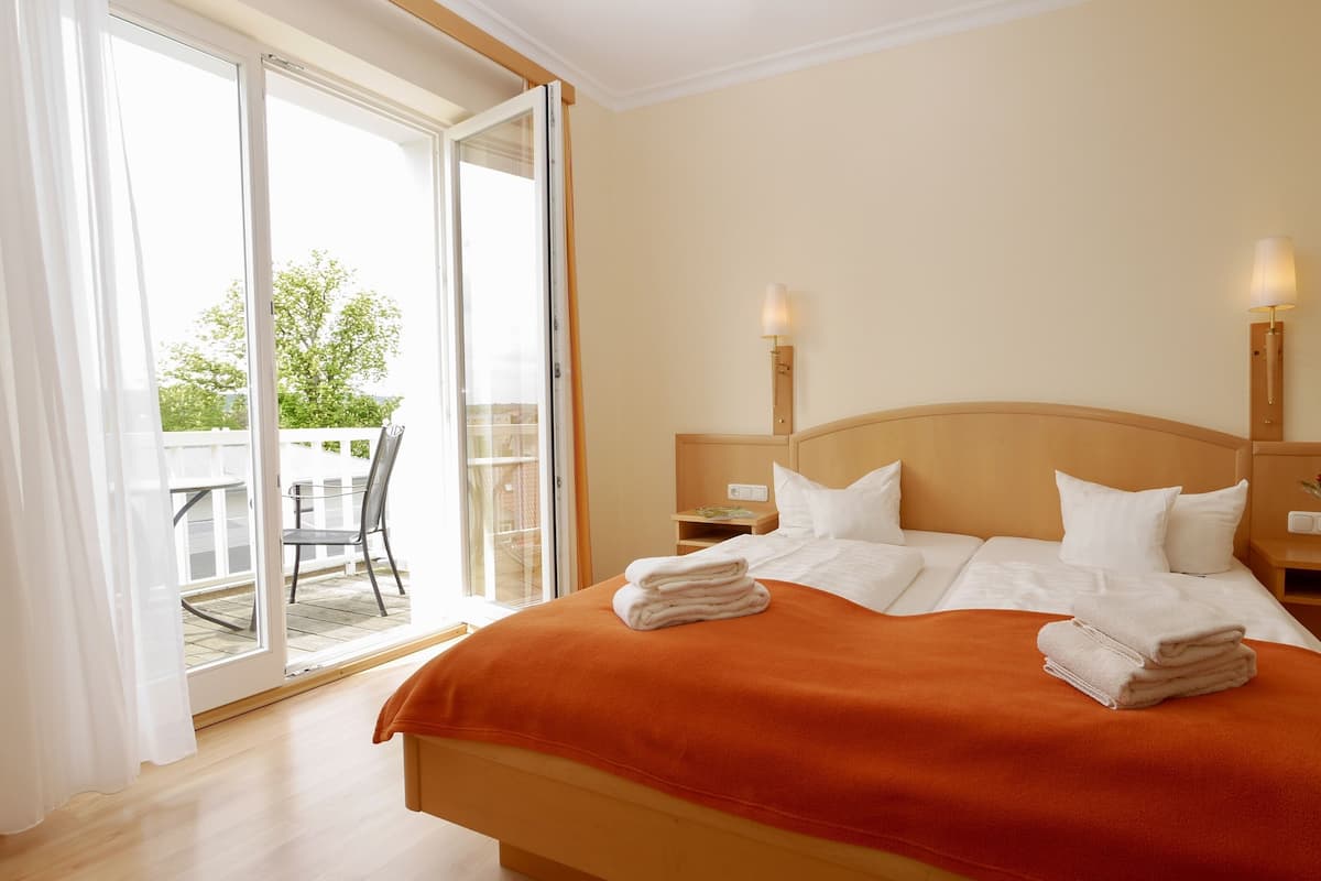 Quarto de hotel com uma cama grande, uma mesa de cabeceira, um abajur e vista para o exterior através de uma porta de correr.