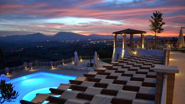 Zona de piscina con una tumbona de cuadros, un pabellón y vistas a montañas distantes al atardecer.