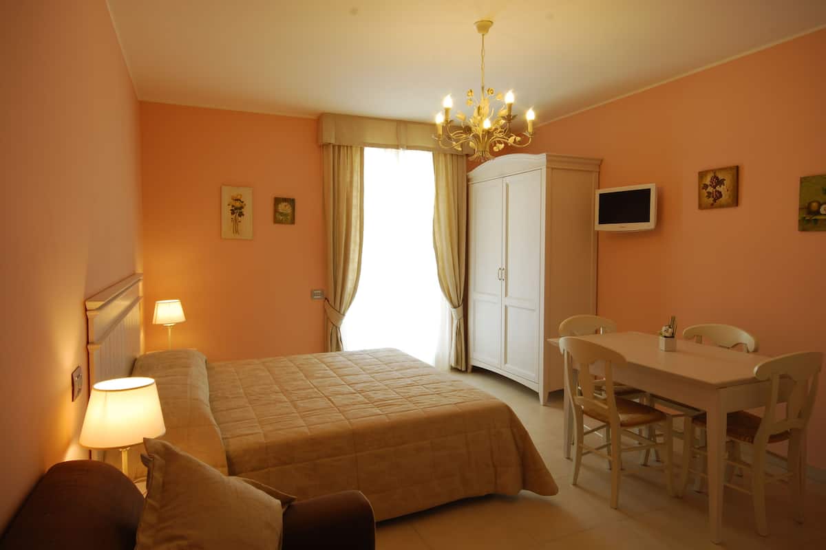 A hotel room with a bed, bedside lamps, a desk with chairs, a television, and a wardrobe.