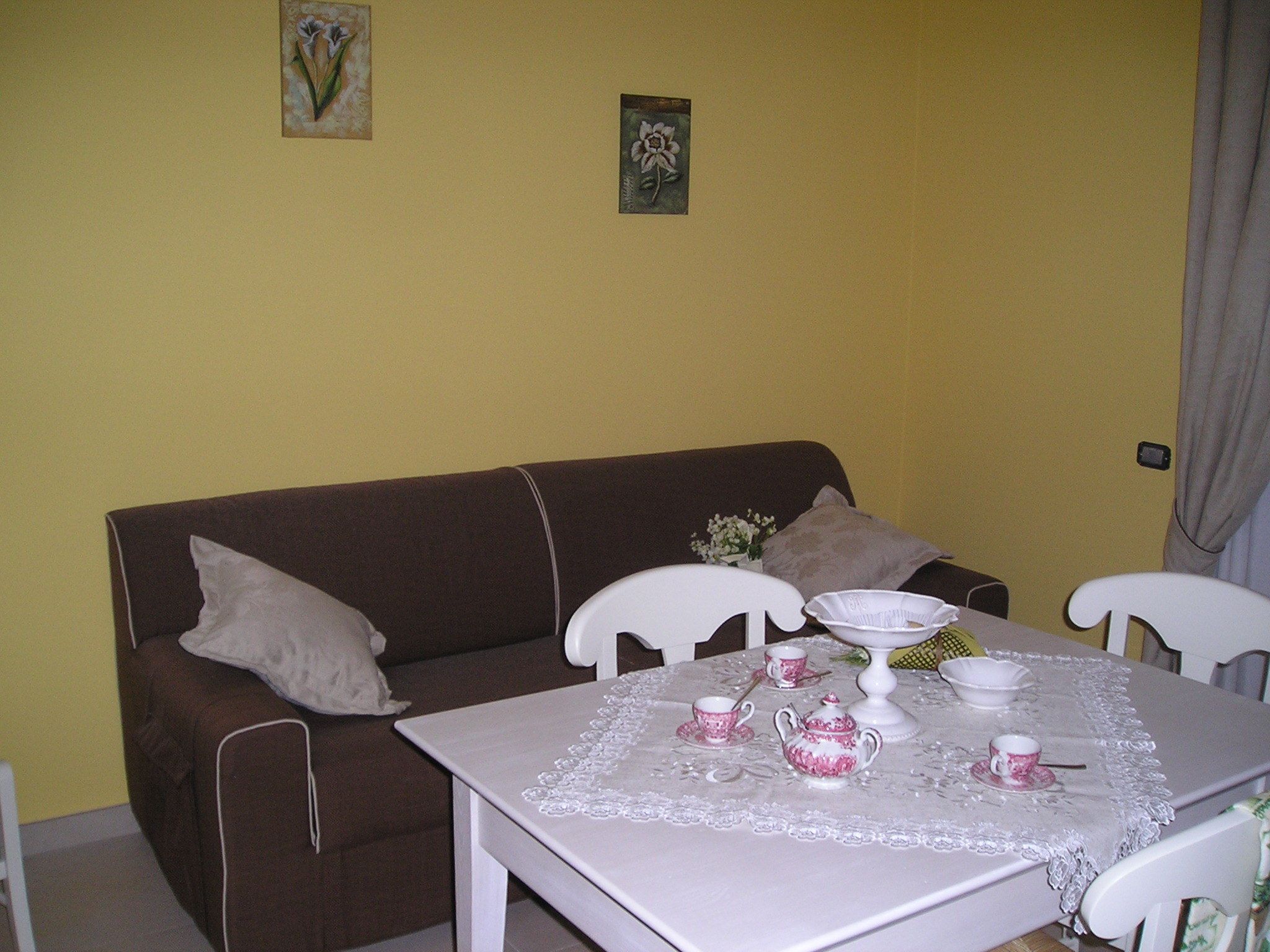 Un pequeño comedor con una mesa lista para dos personas, un sofá marrón y dos sillas blancas.