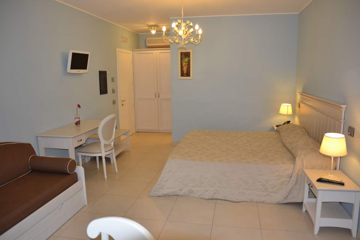 A bedroom with a bed, a desk, a chair, a bedside table with a lamp, a TV, and a wardrobe.