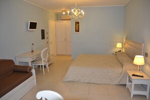 A bedroom with a bed, a desk, a chair, a bedside table with a lamp, a TV, and a wardrobe.
