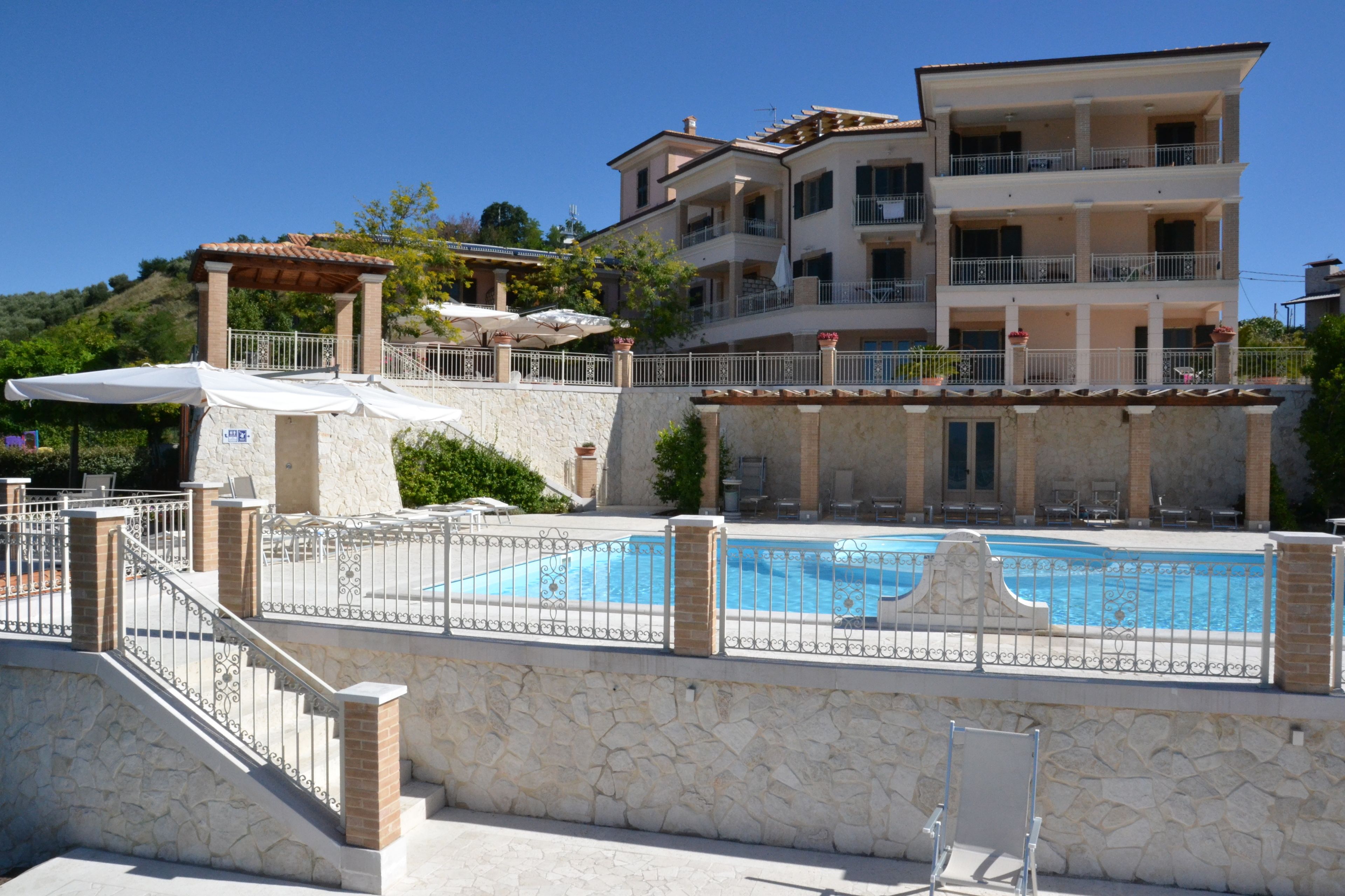 A multi-story hotel with a swimming pool, stone walls, and outdoor seating.