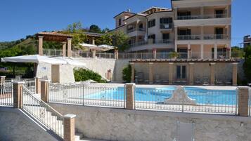A multi-story hotel with a swimming pool, stone walls, and outdoor seating.